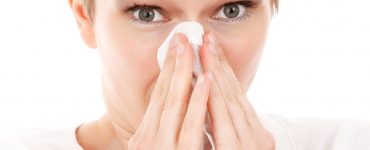 Woman with short hair holding a tissue about to blow her nose