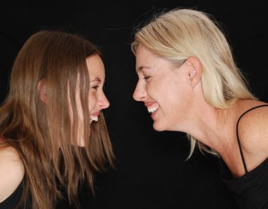 Two woman smiling and looking at each other leant over